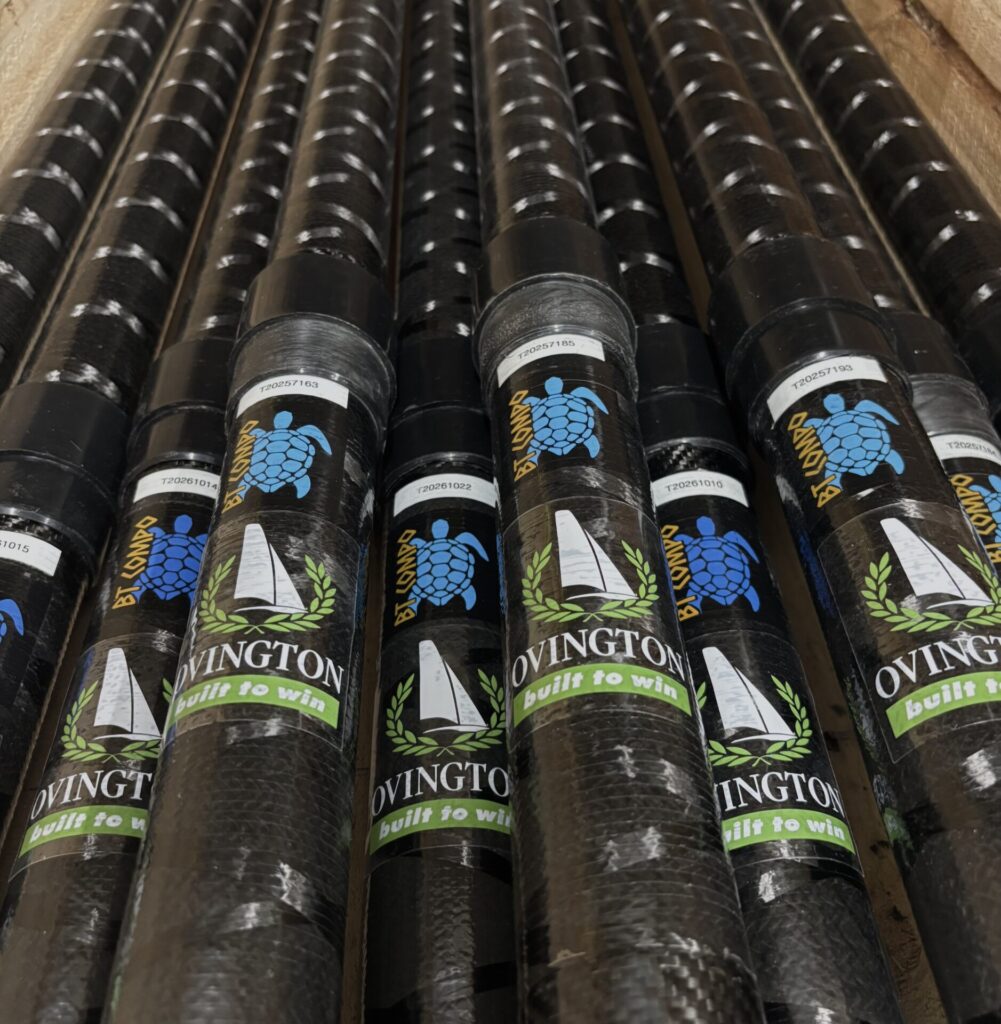 BT Compo top mast - Ovington Boats Multiple black cylindrical pipes lined up side by side with white label bands and a blue turtle logo on each tube